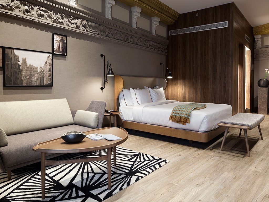 Hotel suite with a curved wood bed frame, oval coffee table and upholstered bench